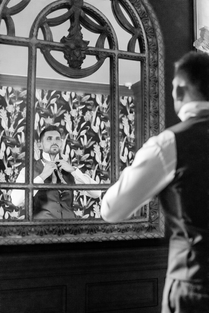 Groom adjusts tie in the library at Rust Manor House