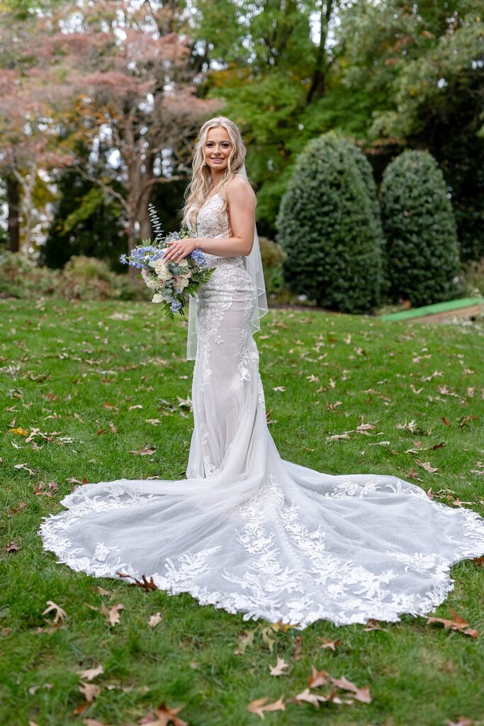 Bride stands holding bouquet fof light blue and cream flowers or portrait on the grounds of the Kurtz Beach cottage in Maryland