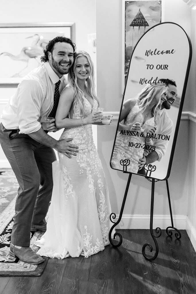 Bride and groom pose by their wedding reception mirrored sign