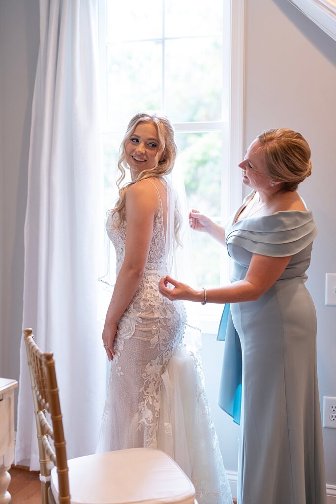 Mother of the bride helps her put on veil by window . Shot by Maryland wedding photographer Nadine Nasby Photography