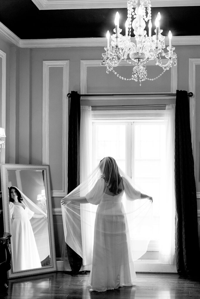 Bride expands veil in front of mirror with antique chandelier hanging above - documentary style wedding photographer DC