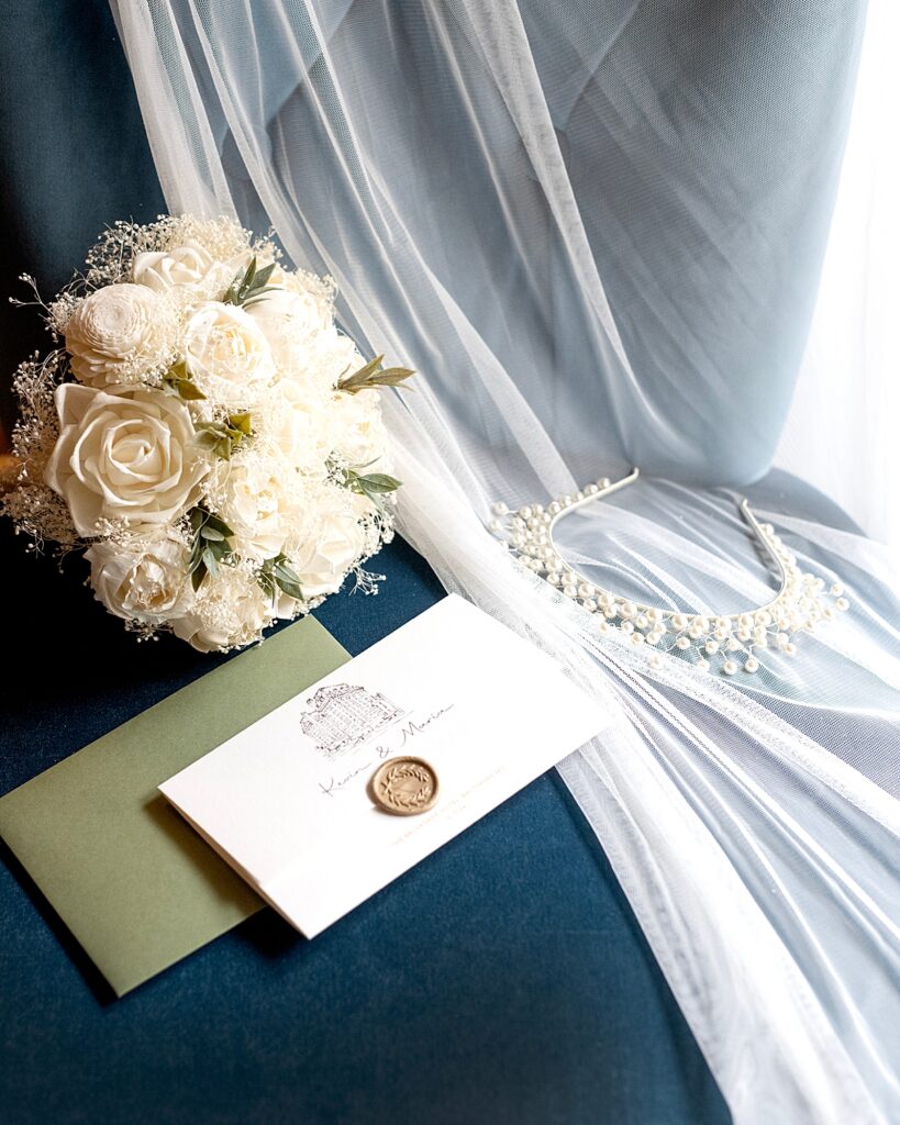 Wedding invitation, veil, bouquet, and headpiece on blue velvet chair - 