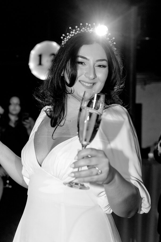 Bride smiles and lifts her champagne flute toward camera - documentary style wedding photographer DC.